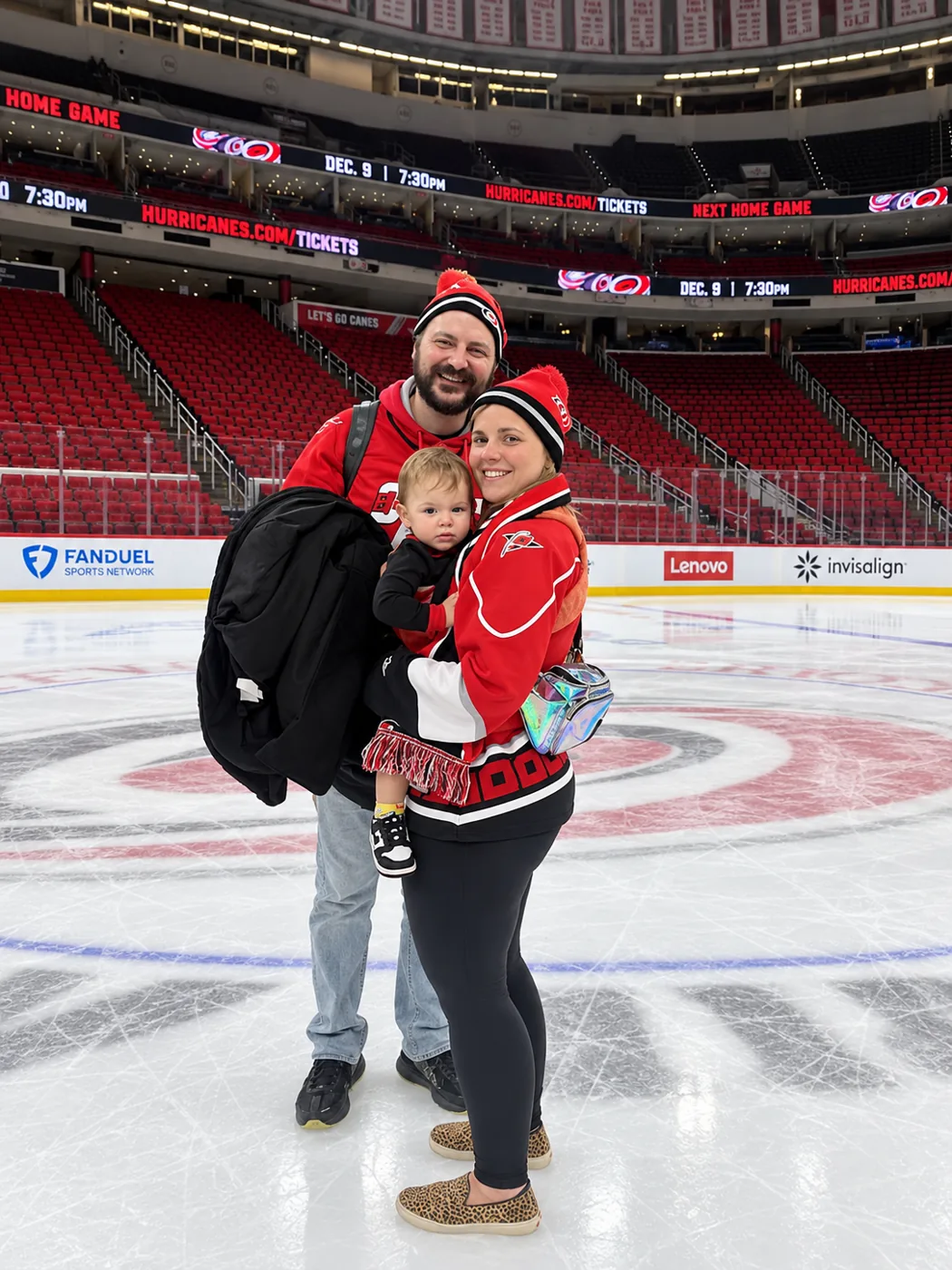Adam, his wife and their toddler in Hurricanes gear, standing on the ice at center rink in an empty arena