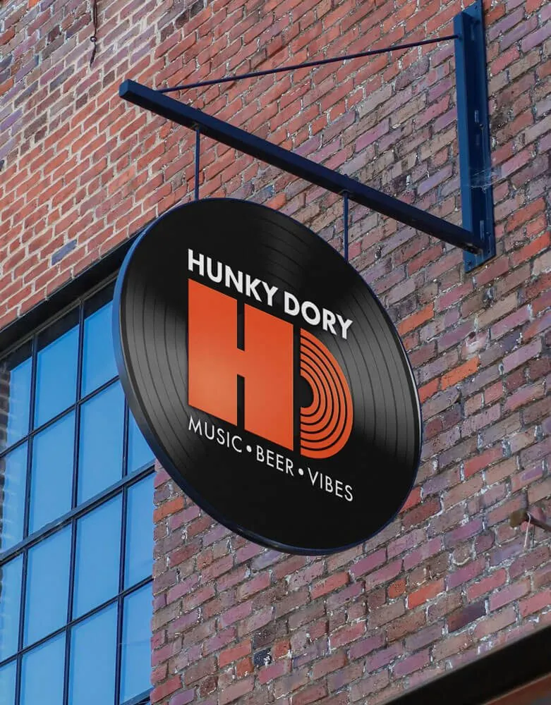A round Hunky Dory sign shaped like a vinyl record, hanging from a brick building