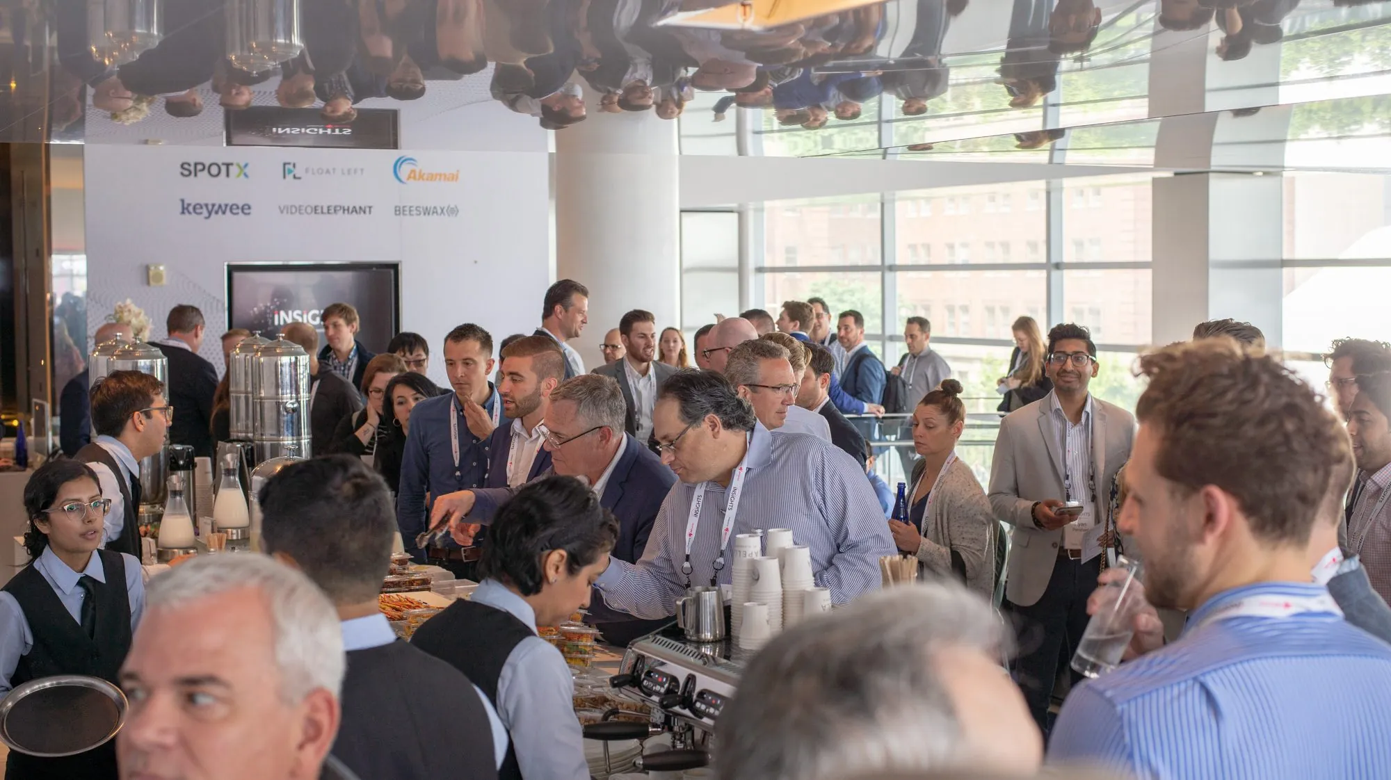 Guests at a busy coffee bar in front of the Insights sponsor wall and branded screens