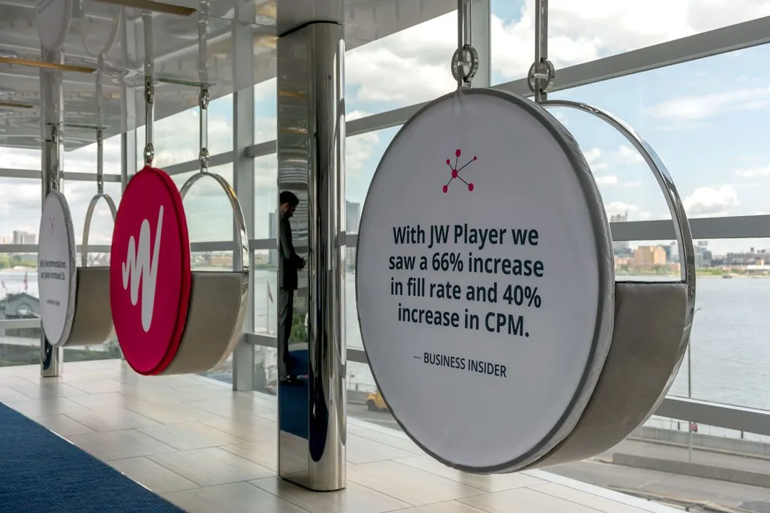 Round hanging signs over the river, one with the W and one quoting Business Insider’s results with JW Player