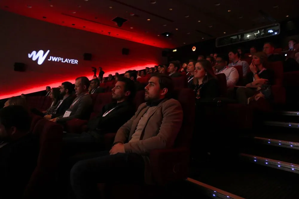An Insights audience in a red-lit London cinema, the JW Player logo on the screen