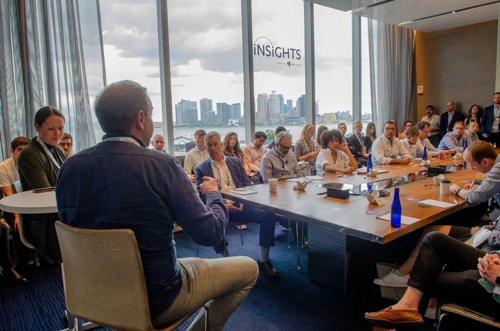 A packed roundtable session in front of floor-to-ceiling windows, the Insights logo on the glass