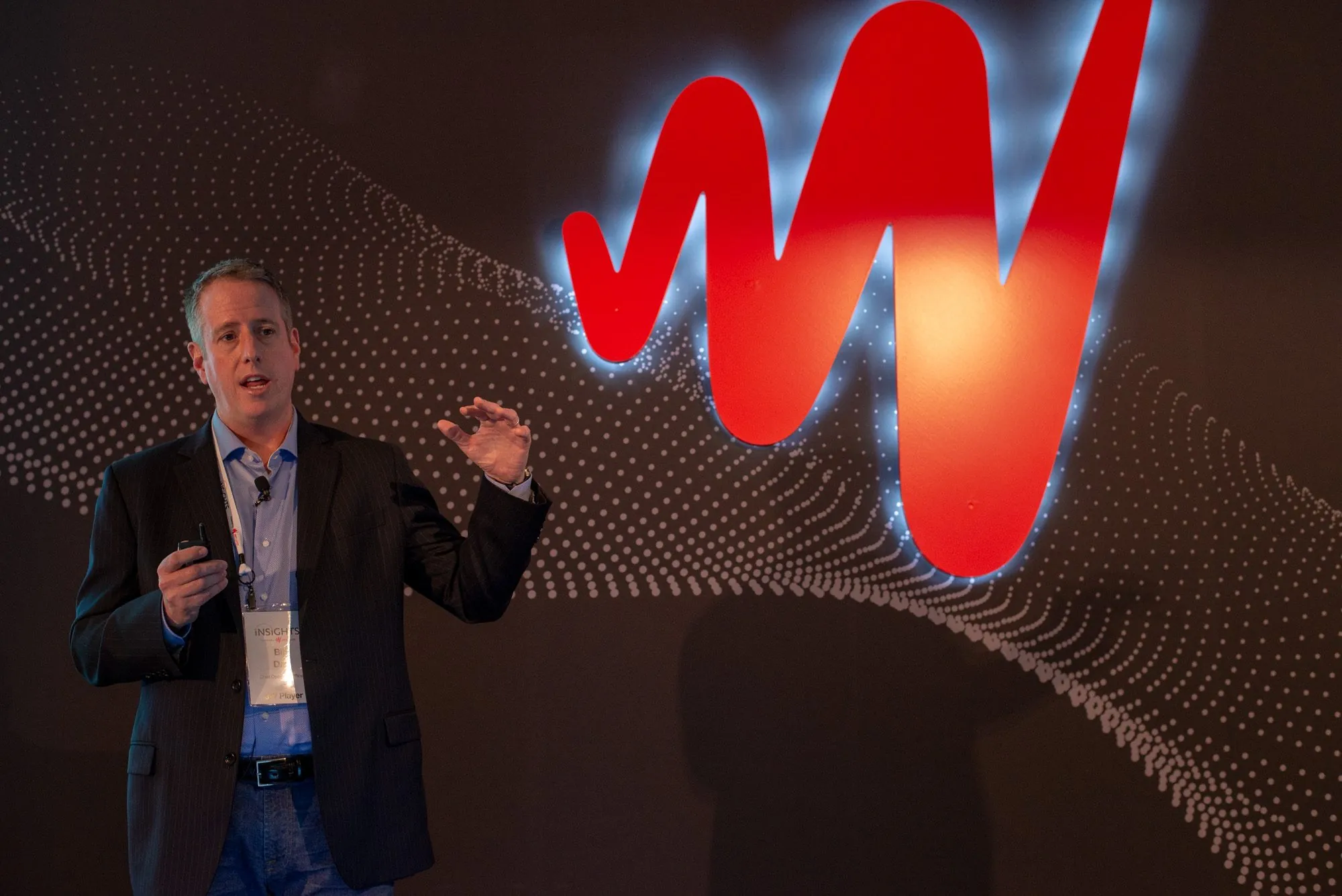 A speaker on stage in front of a backlit red W and a wave of white dots