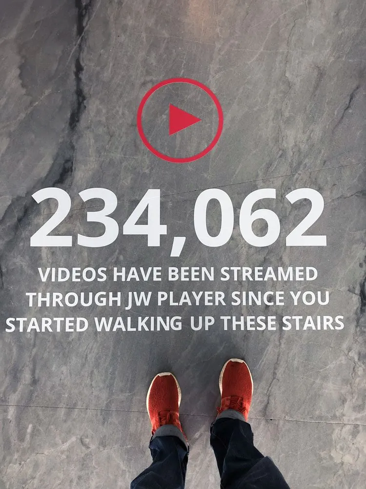 A floor graphic at the top of the stairs: 234,062 videos have been streamed through JW Player since you started walking up these stairs