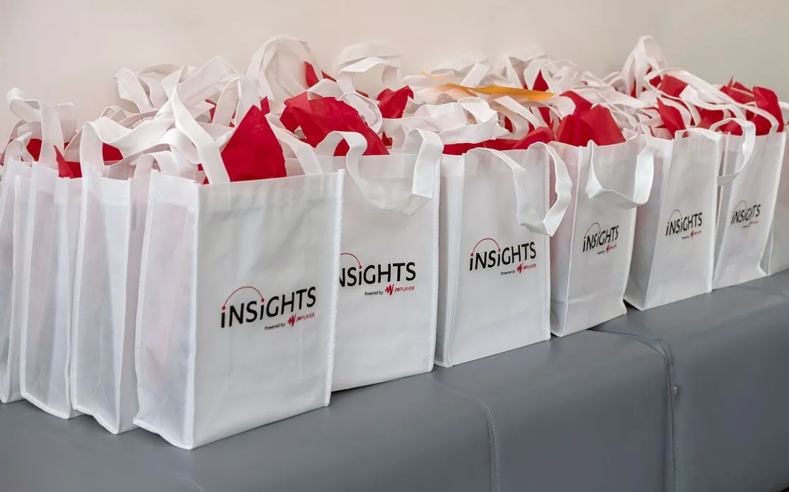 A row of white Insights tote bags stuffed with red tissue paper