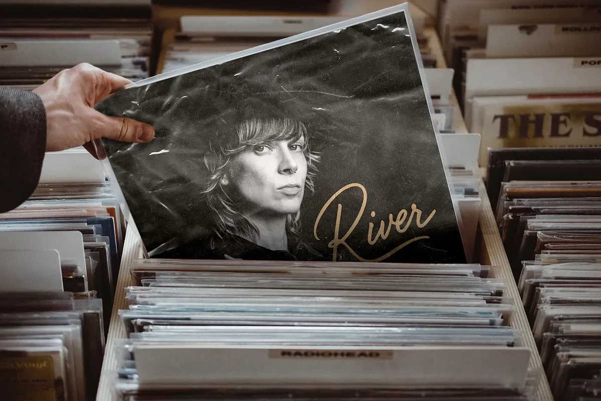 River album cover in a plastic sleeve being pulled from a record bin, black and white portrait with gold script lettering