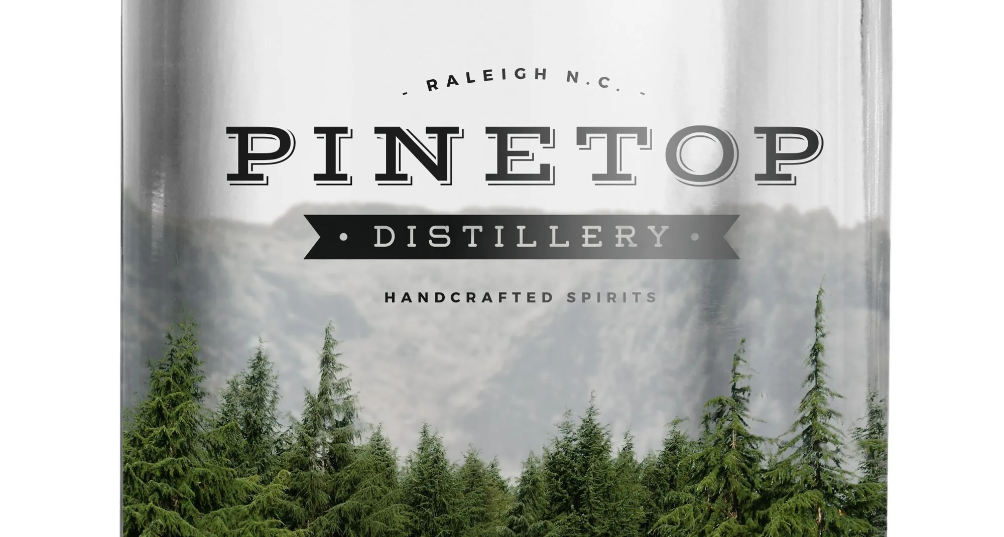 A rendering of the clear Carolina Moonshine front label on a bottle: the Pinetop logo over misty mountains, with a stand of pines along the bottom