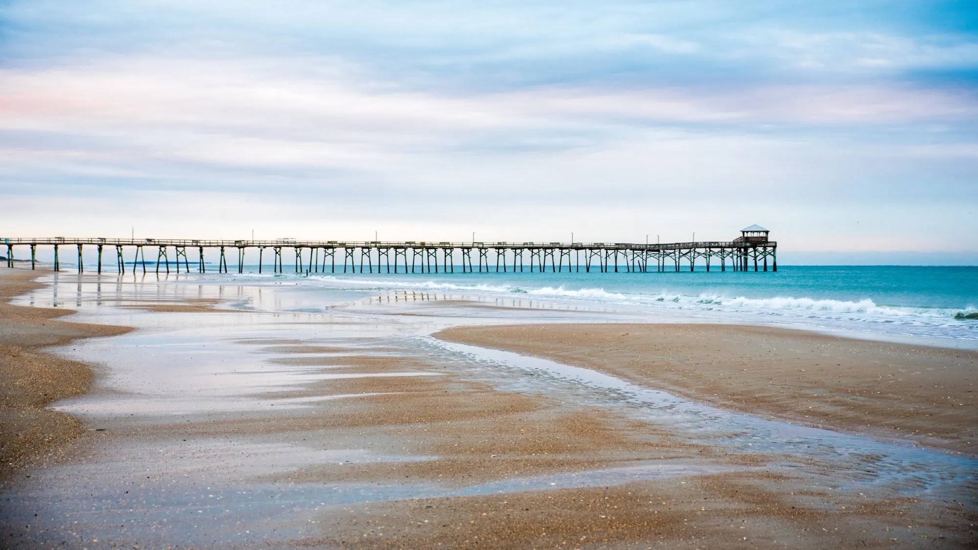 A long wooden fishing pier stretching into a turquoise sea at low tide