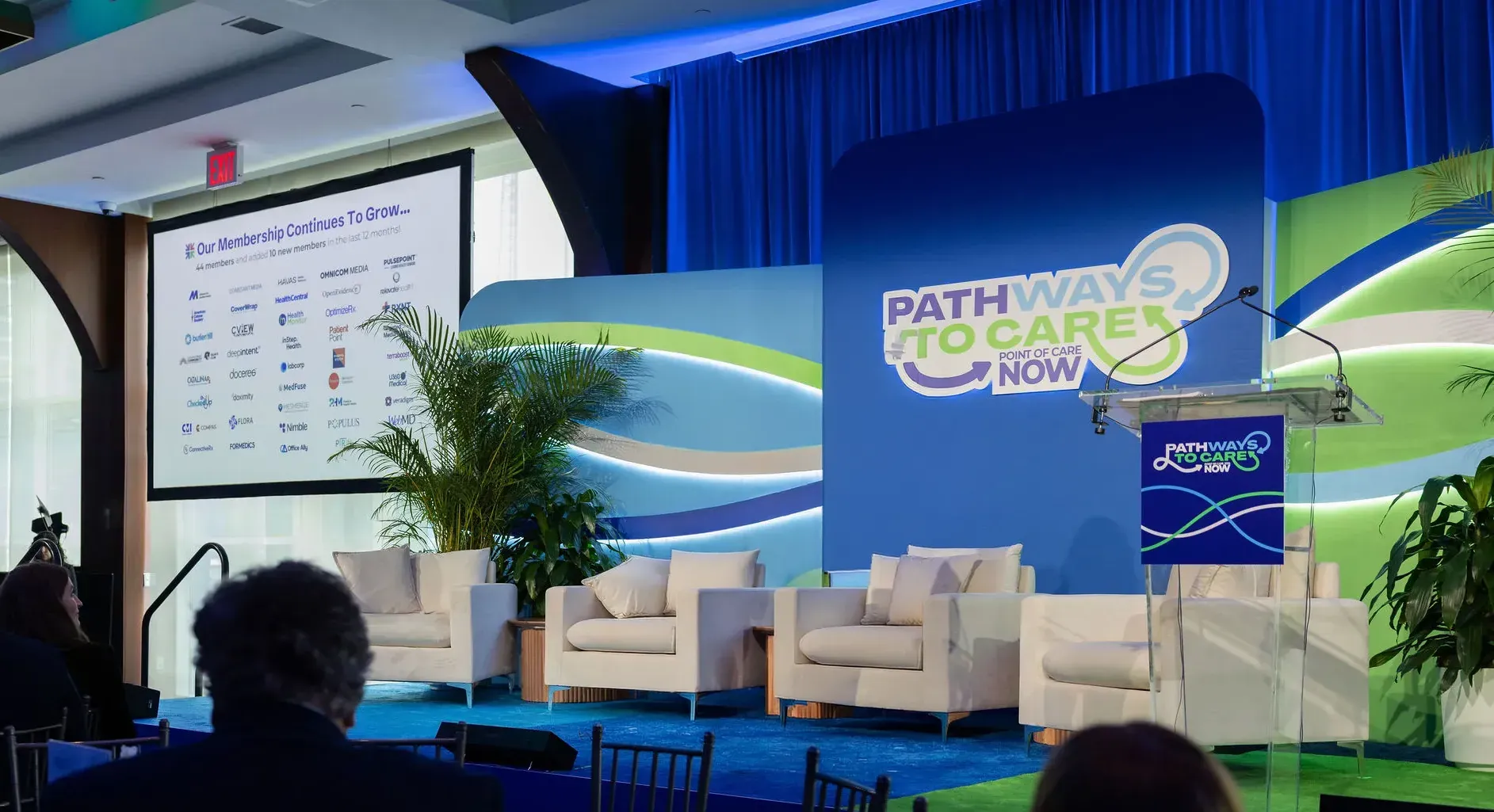 The main stage during a session: the looping logo lit on the stage wall, the podium in front and a slide on the side screen