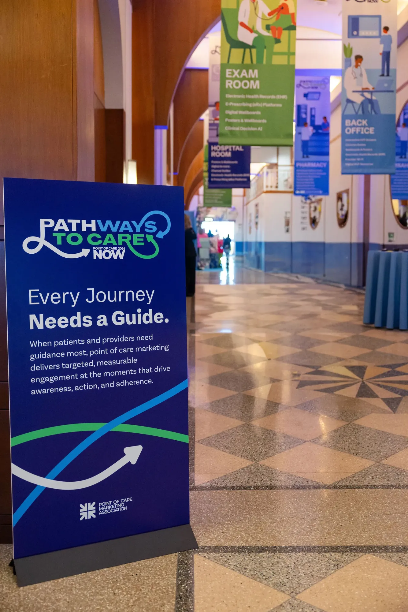 An entrance sign reading Every Journey Needs a Guide, with the logo above and the loop’s arrow swooping across the bottom, the hanging banners behind it