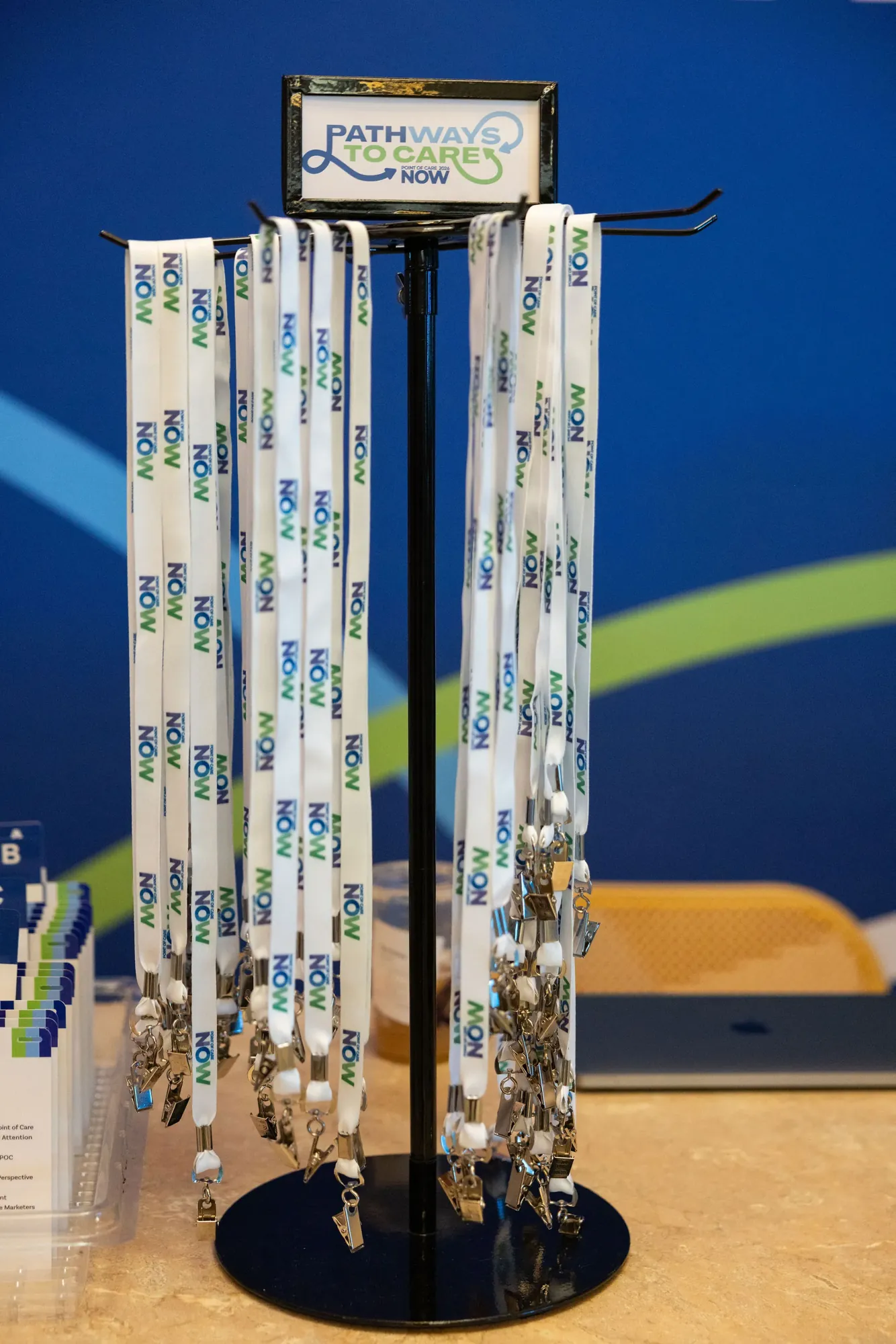 White lanyards printed with NOW in blue and green, hanging from a rack under a small Pathways to Care sign