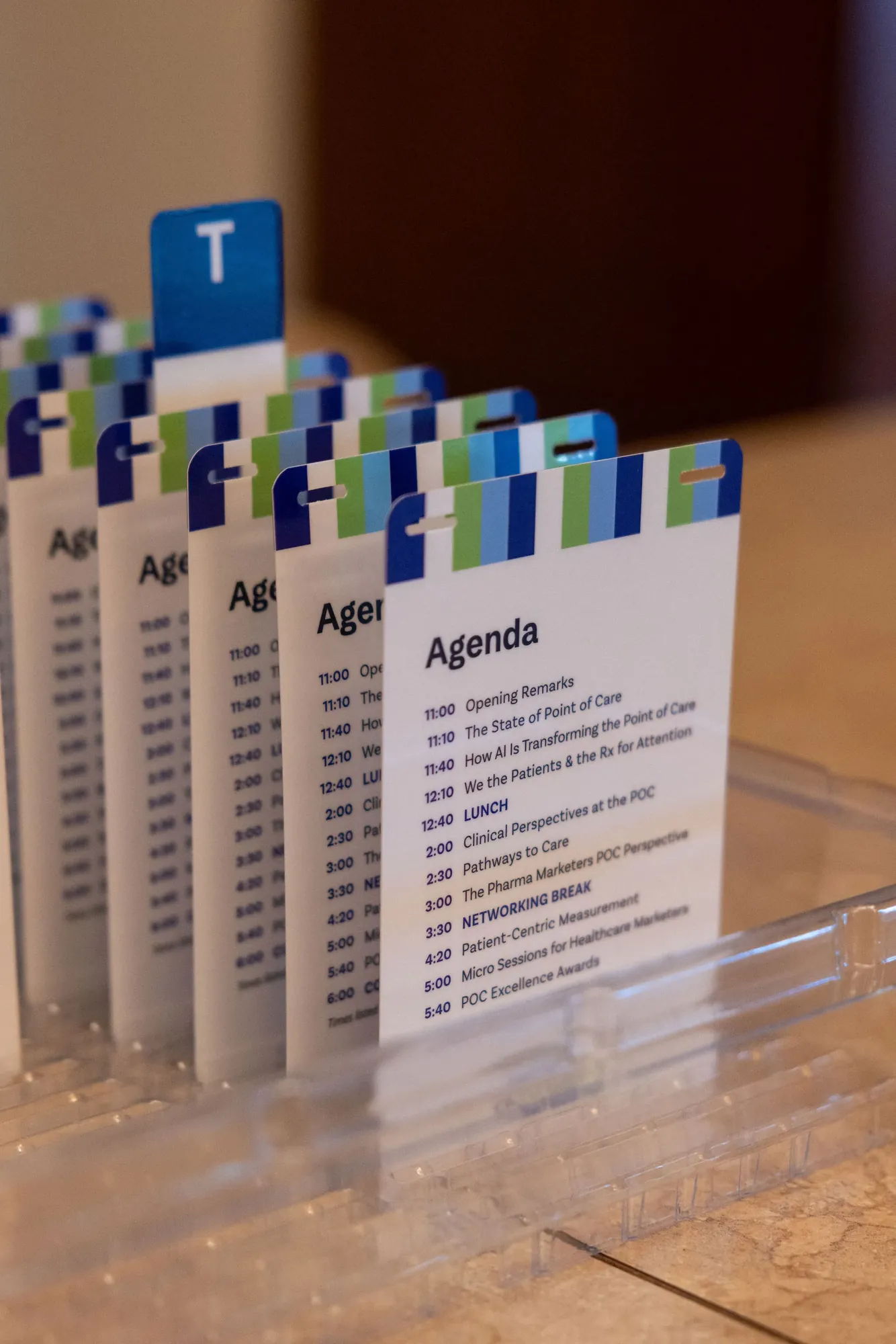 A row of agenda cards cut like badges, each with a striped blue and green top and the day’s sessions from 11:00 to 5:40